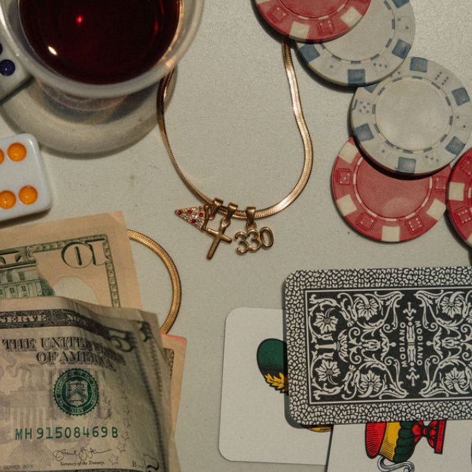 Casino-themed items, including poker chips, dice, a card, and a glass of red wine on a table with a Youngstown, Ohio Necklace featuring a 330 charm, a cross charm, and a pizza charm.