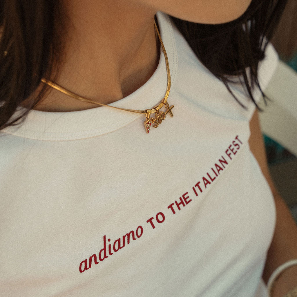 Person wearing a white shirt with red text 'andiamo TO THE ITALIAN FEST' and gold jewelry.
